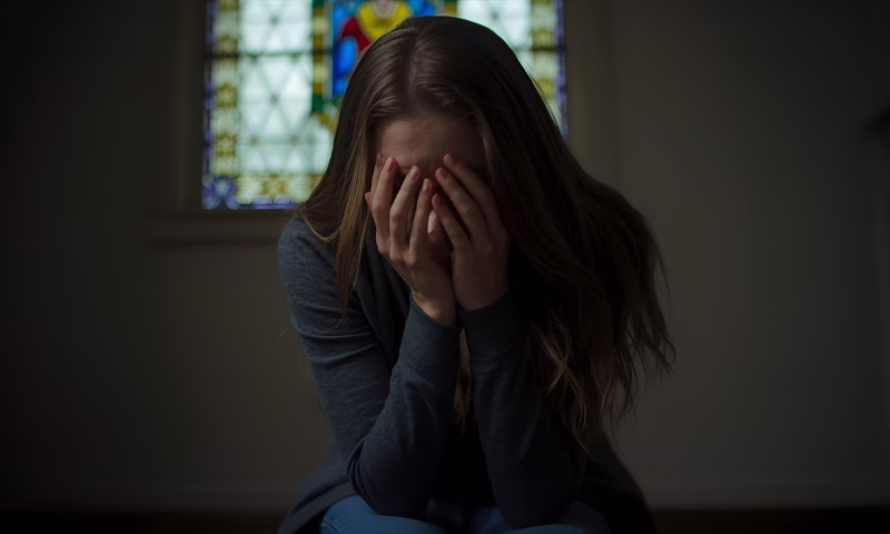 Jovem, mulher, em crise de ansiedade, com as mãos no rosto.